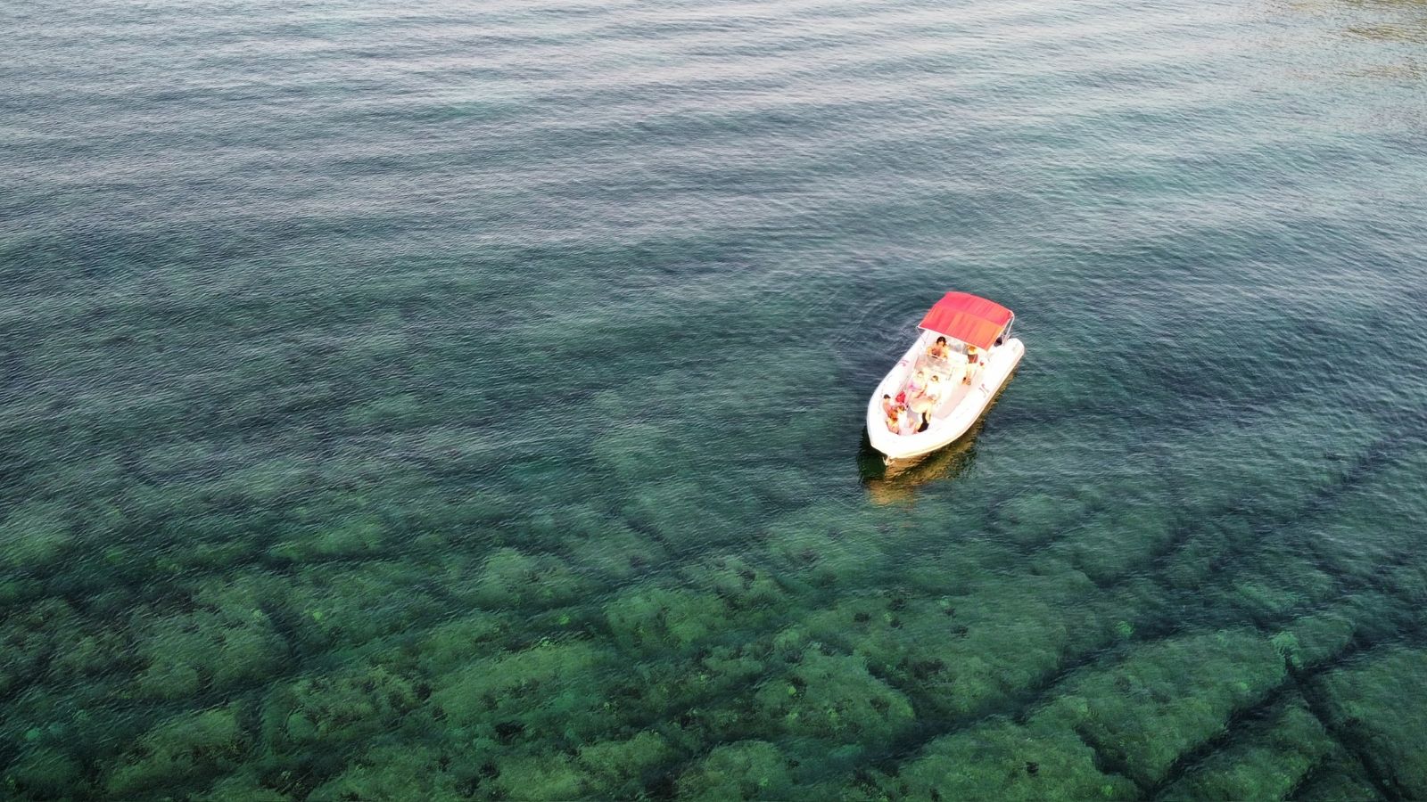 Gommone con tendalino rosso ancorato su fondale roccioso