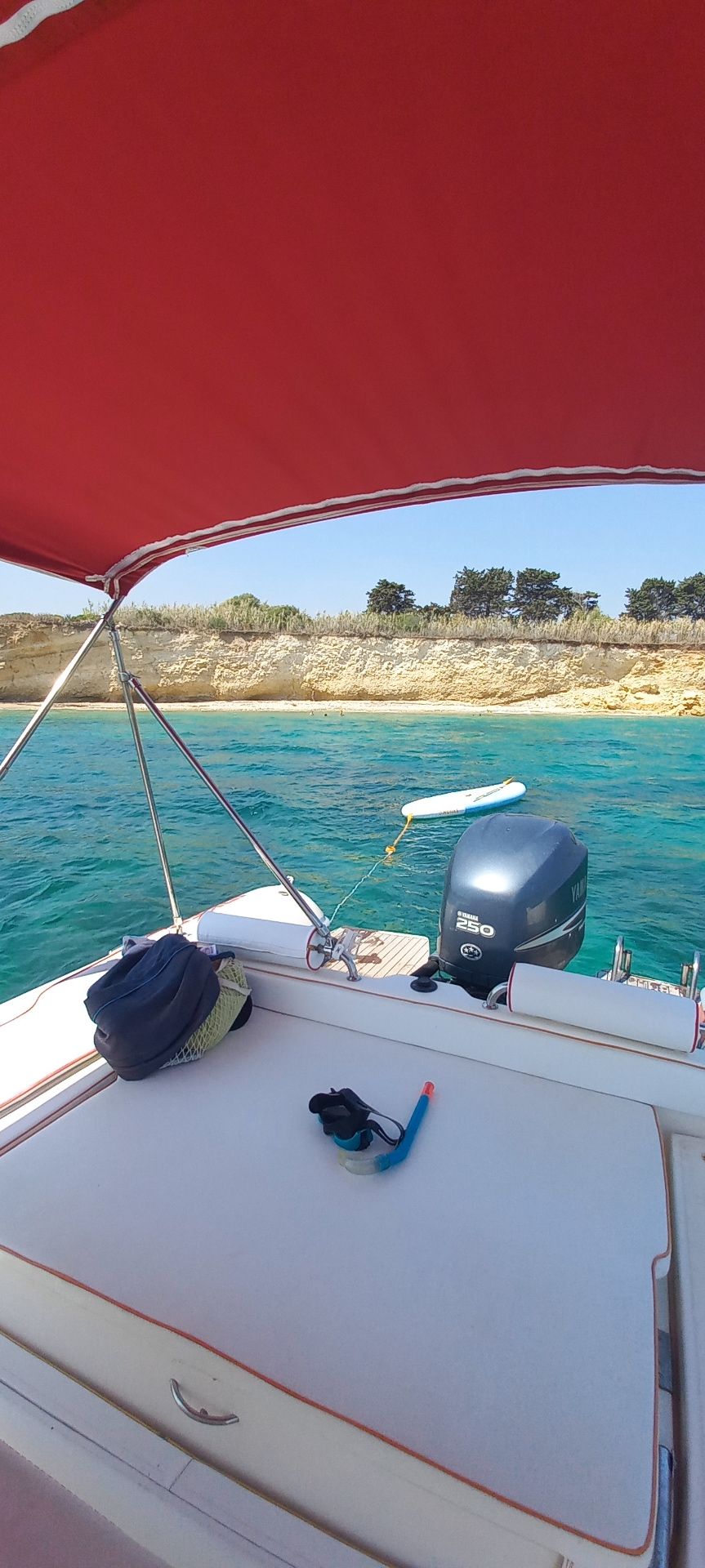 Vista dal gommone con tendalino rosso su caletta turchese